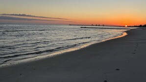 A beach with a pier extending into the water, a clear sky, and footprints on the sand.