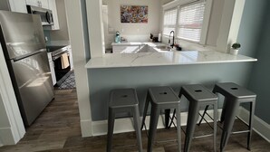 A modern kitchen with a marble countertop, stainless steel appliances, and a bar stool seating area.
