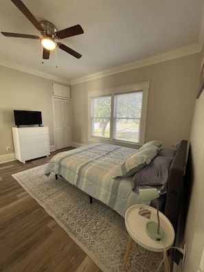 A bedroom with a bed, a ceiling fan, a TV on a dresser, and a window with blinds.