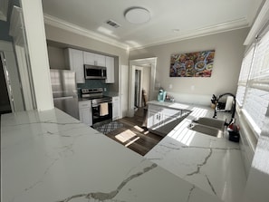 A modern kitchen with white cabinets, stainless steel appliances, and a marble countertop.