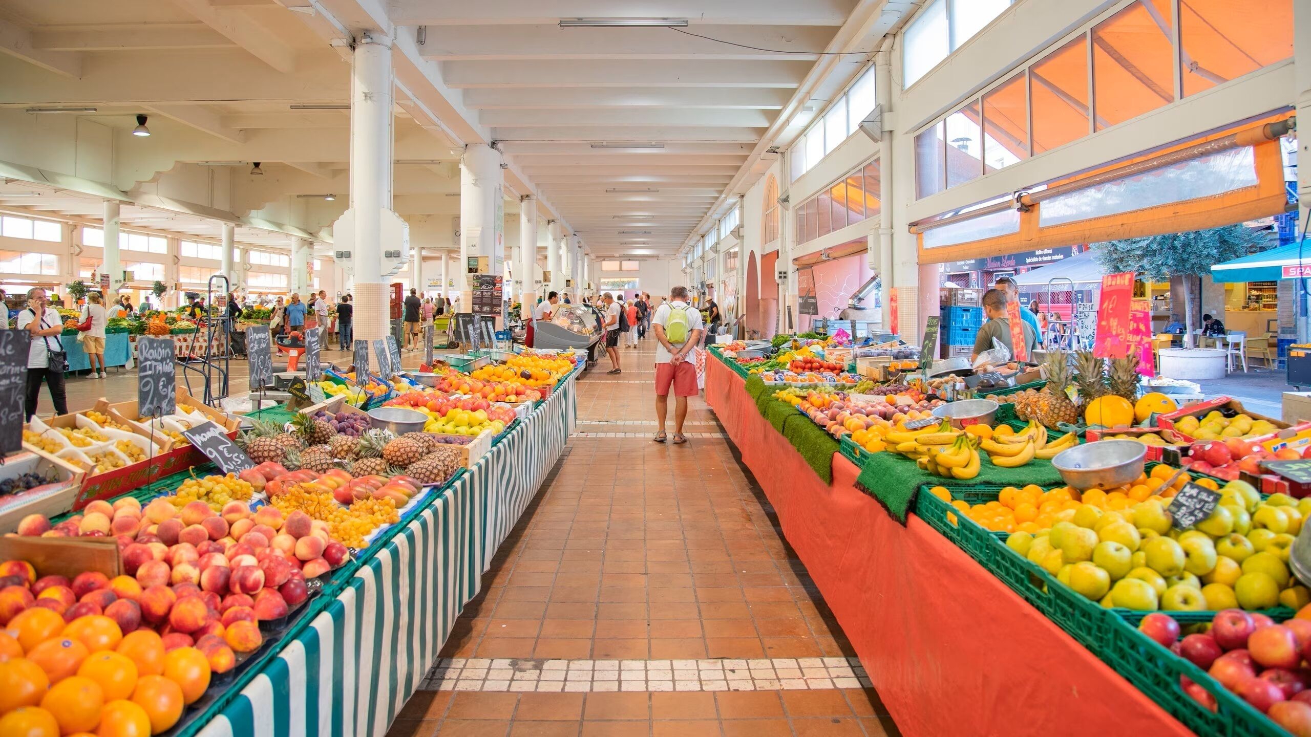 Een ruime overdekte markt met brede gangpaden en hoge plafonds, met diverse kraampjes vol verse producten.