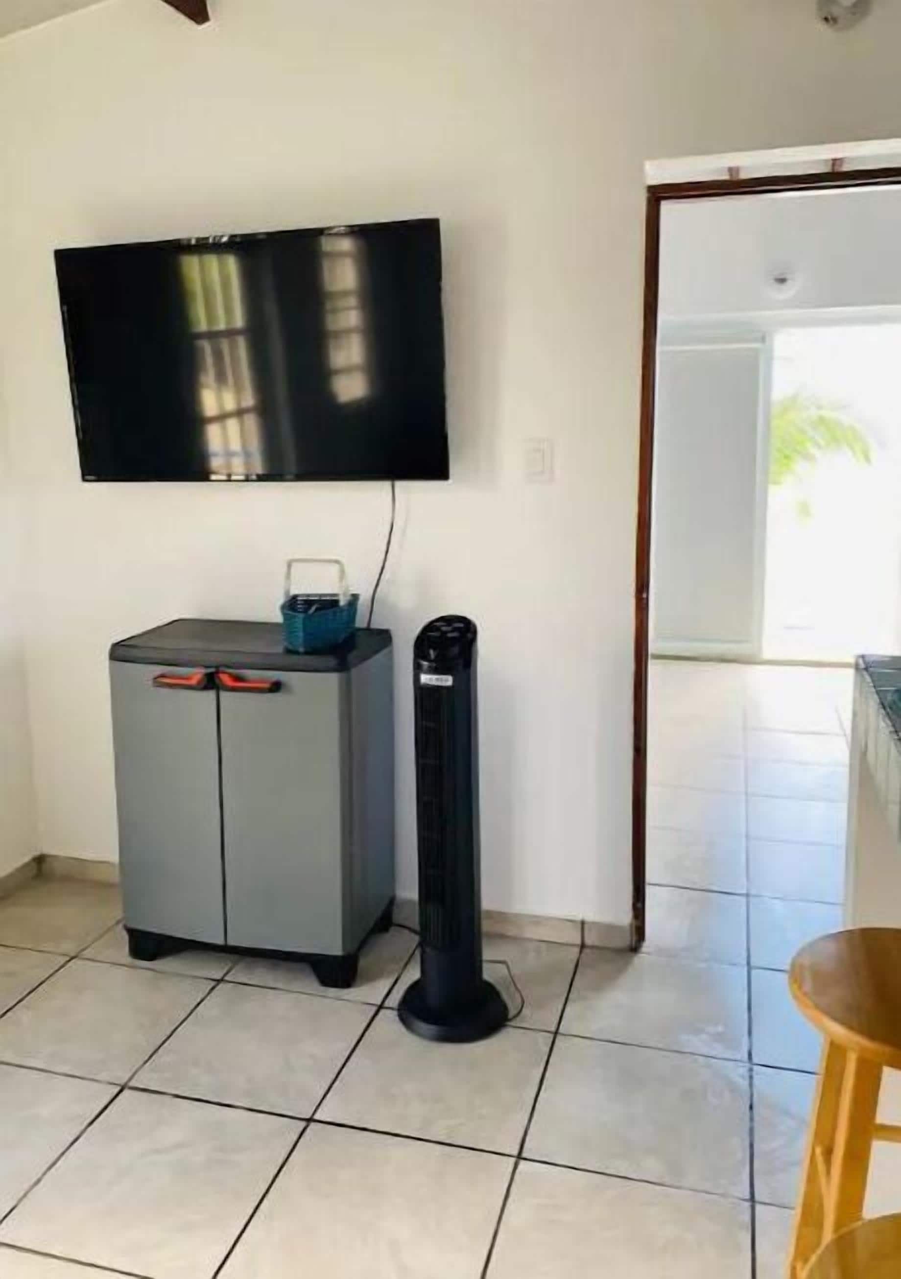 A room with a tiled floor, a grey cabinet with red handles, a black standing heater, and a flat-screen TV mounted on the wall.