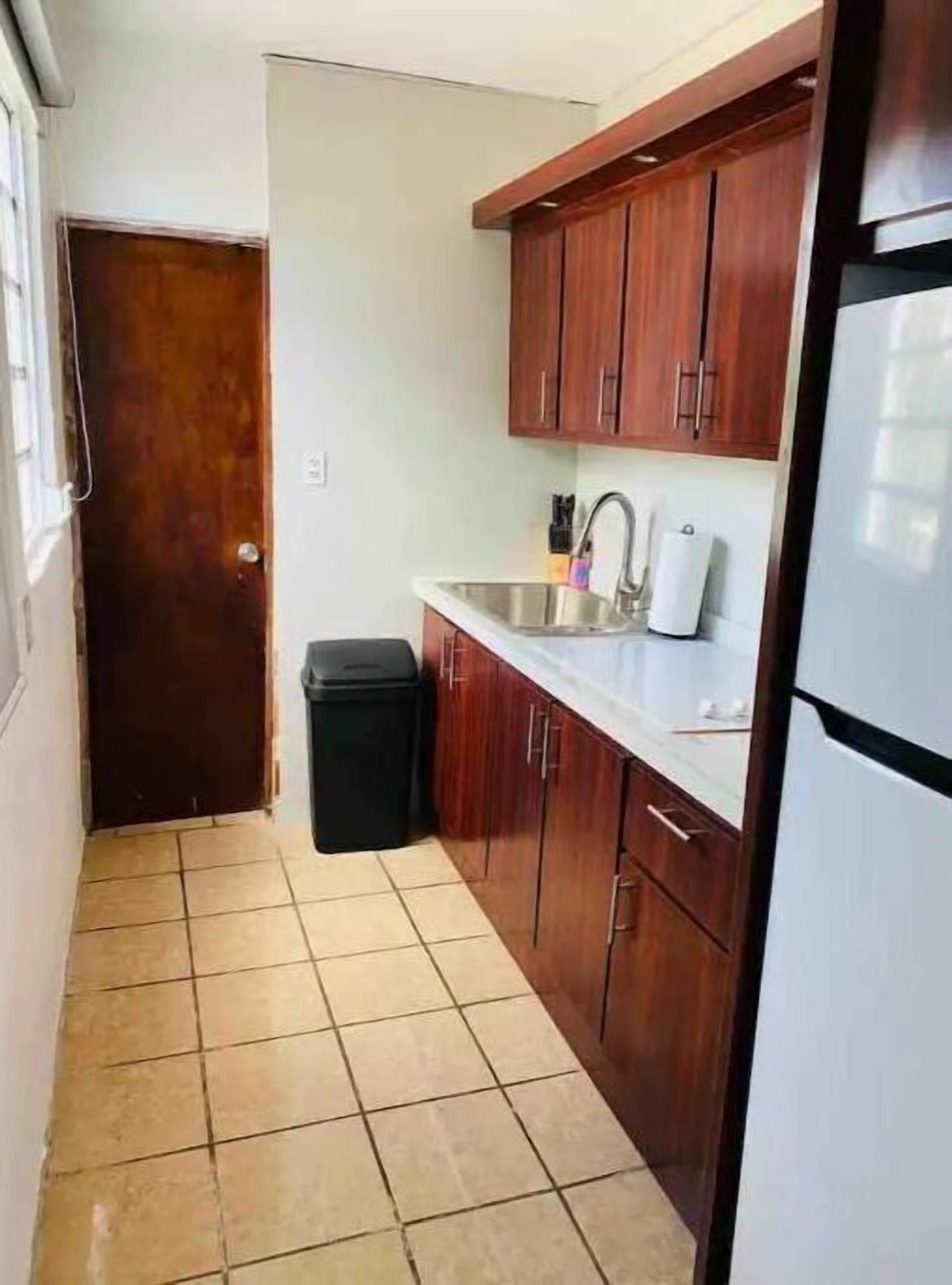 A compact kitchen with wooden cabinets, a stainless steel sink, and a refrigerator.