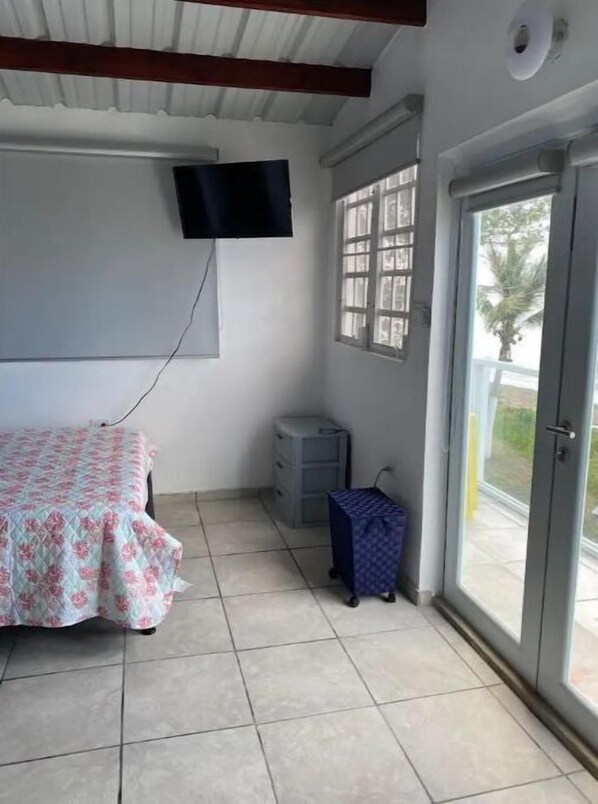 A room with a bed, a television mounted on the wall, a window with a view, and a door leading outside. - Beachfront Full House (Guayama)