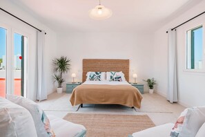 A spacious bedroom with a large bed, two bedside tables, a hanging light fixture, and a view through a sliding door. - Casa Carmela, a charming house in Cala Ferrera (Cala d'Or)