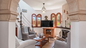 Ein Wohnzimmer mit steinbogigem Durchgang, Kamin, Fernseher und Treppe.