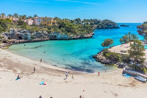 A beach with clear turquoise water, sandy shore, and buildings in the background. - Casa Carmela, a charming house in Cala Ferrera (Cala d'Or)