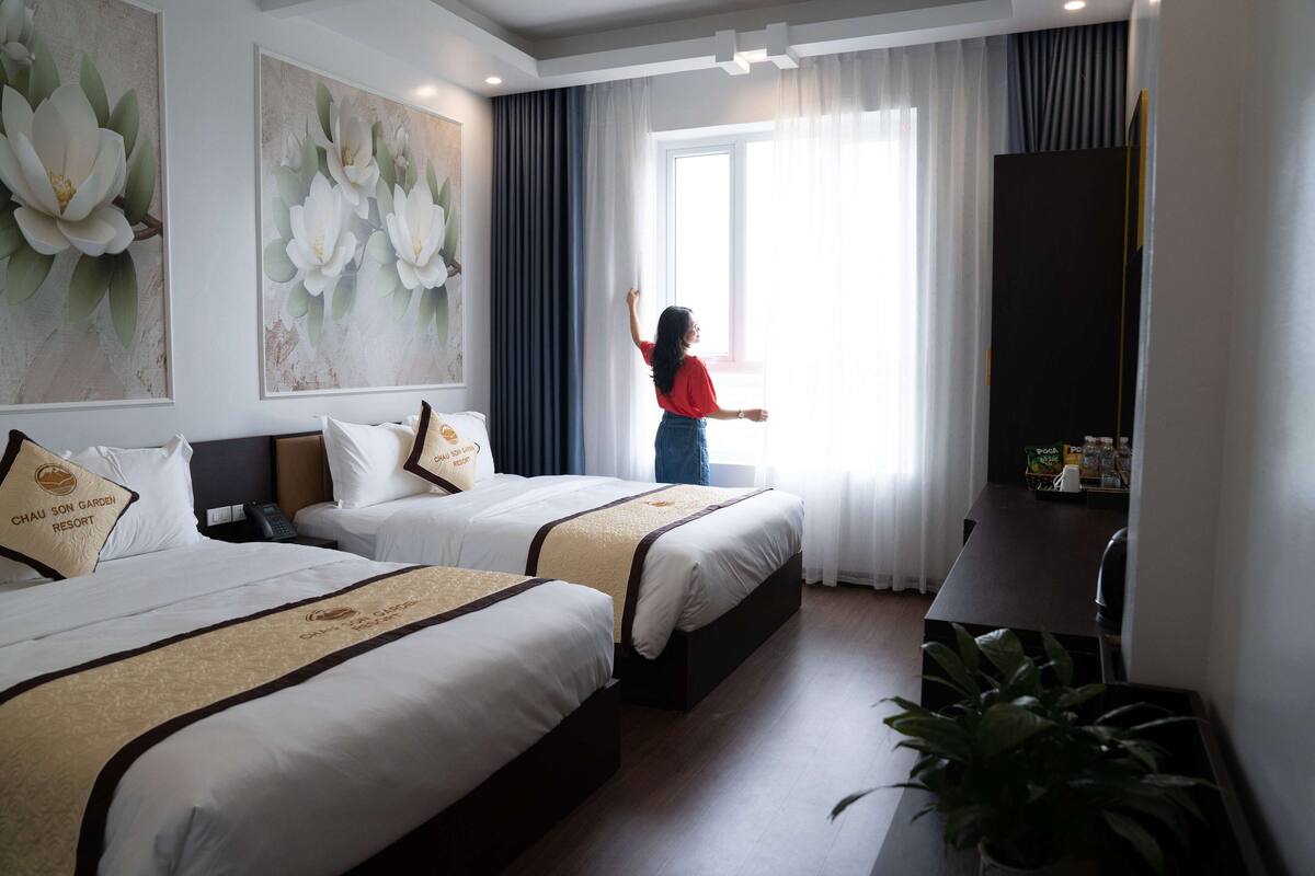 A hotel room with two beds, a desk, and a large window with curtains.
