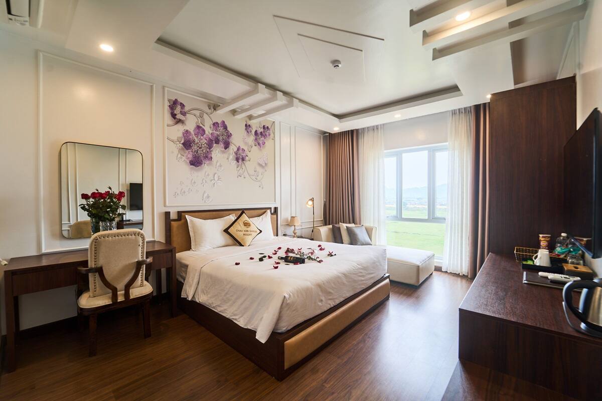 A hotel room with a large bed, a desk, a chair, a mirror, and a window with a view of the outdoors.