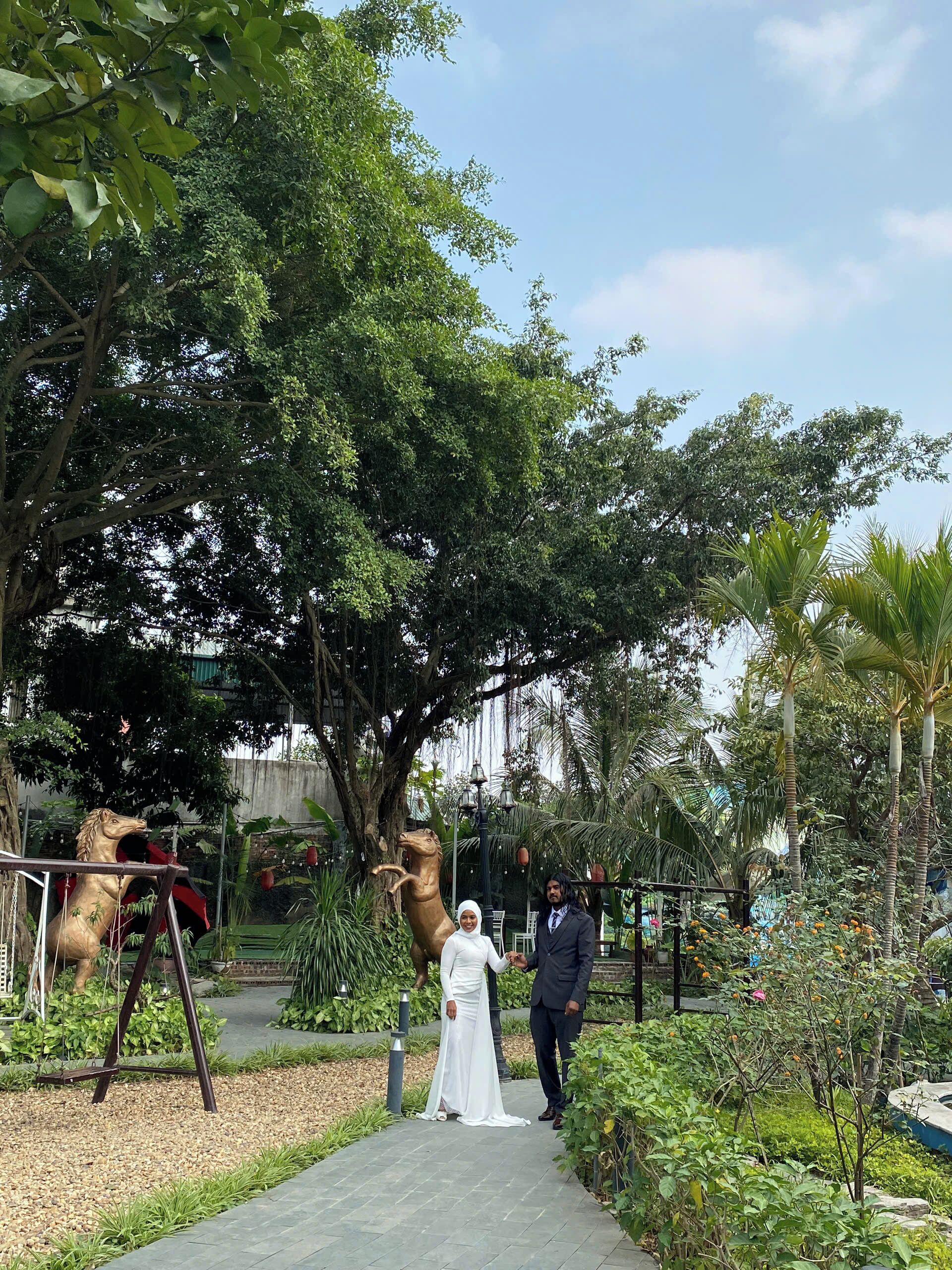 Un sendero en un jardín con una estatua de un caballo, una pareja y abundante vegetación.