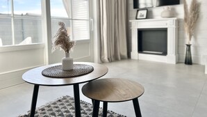 Uma sala de estar moderna com lareira, uma mesa redonda com um vaso de capim-dos-pampas secos e uma televisão na parede.