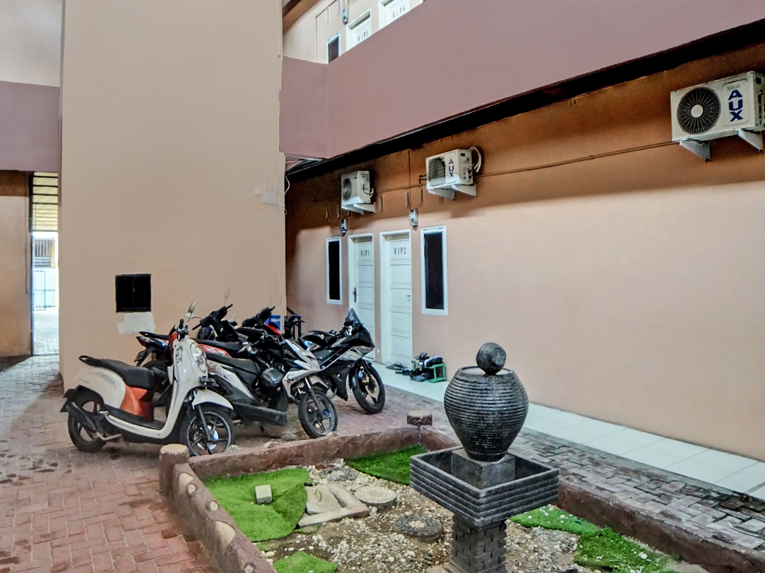 A courtyard with multiple parked scooters, a decorative stone planter, and air conditioning units on the wall.