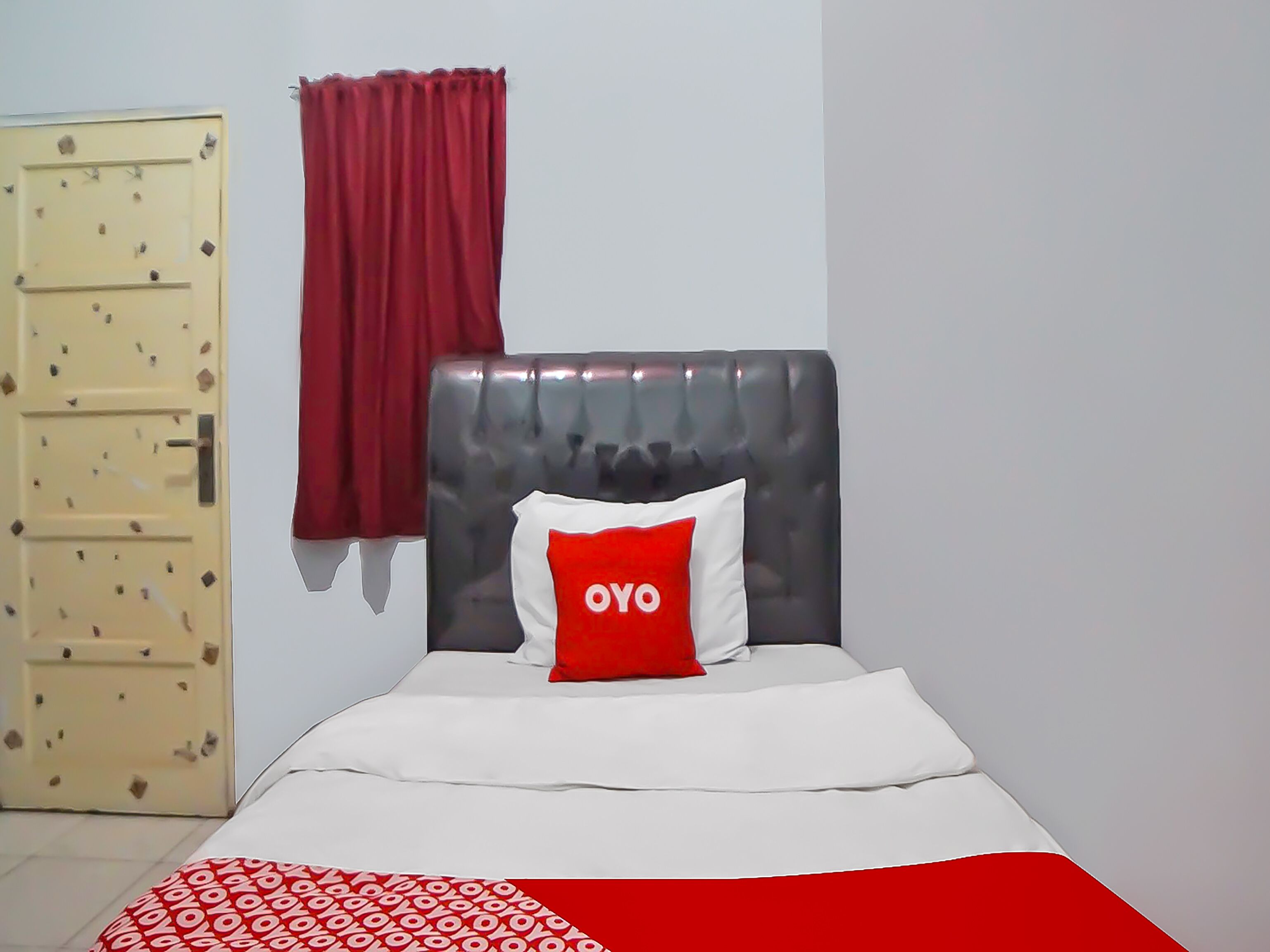 Una habitació amb un llit, una cortina vermella i una porta amb forats de bala.