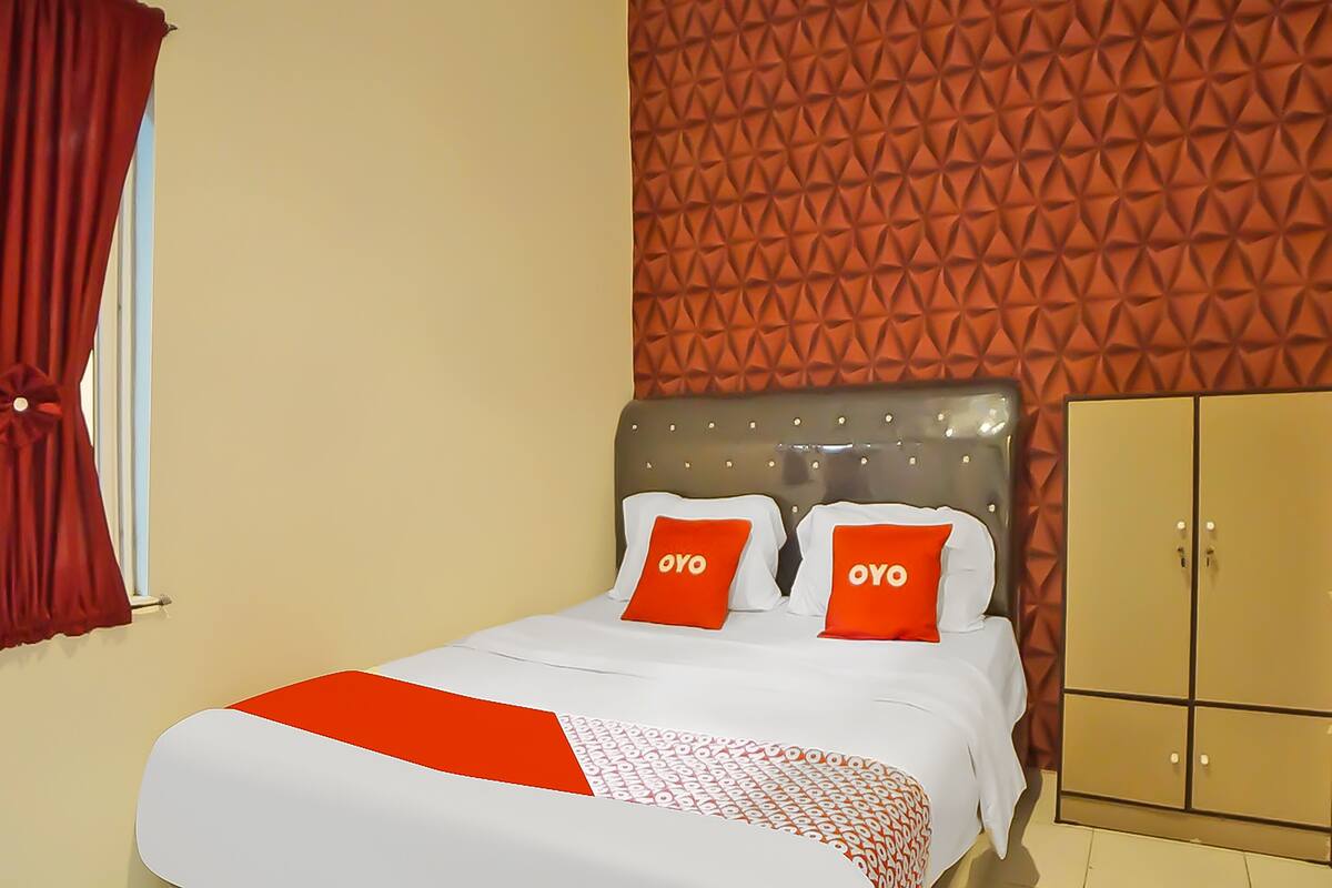 Hotellihuone, jossa on sänky, kaksi «OYO»-logolla varustettua tyynyä, punainen verho, geometrisesti kuvioitu seinä ja vaatekaappi.