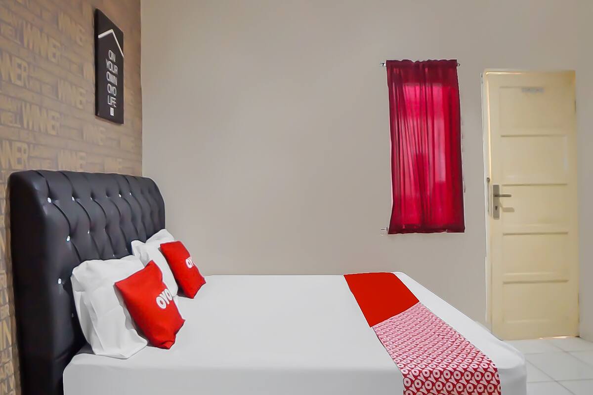 Hotellihuone, jossa on sänky, punavalkoinen kuviollinen päiväpeite, musta pääty ja punainen verho.