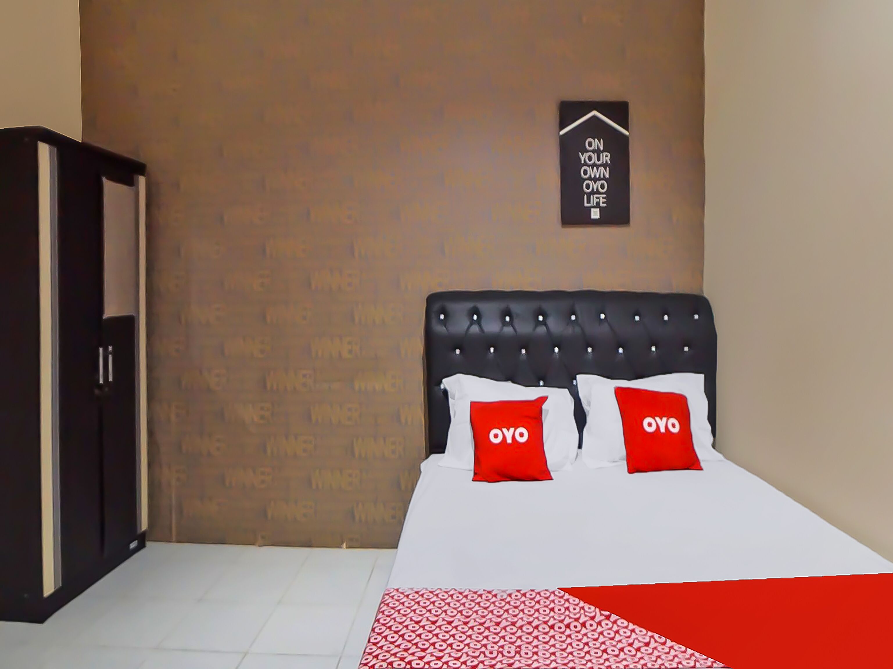 A bedroom with a bed, two pillows with 'OYO' branding, a wall-mounted sign, and a wardrobe.