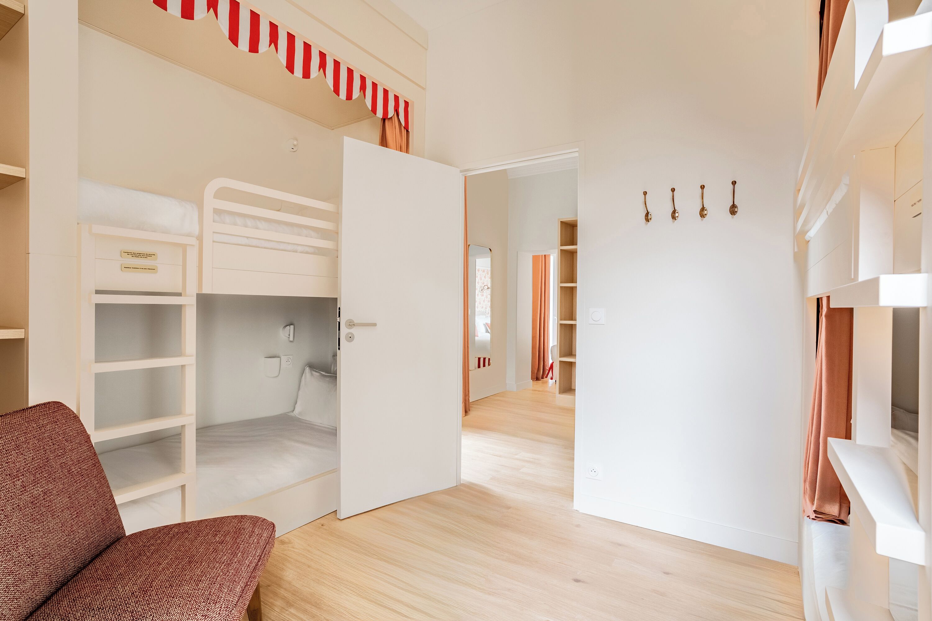 Una habitación con literas, una silla roja y un armario blanco.
