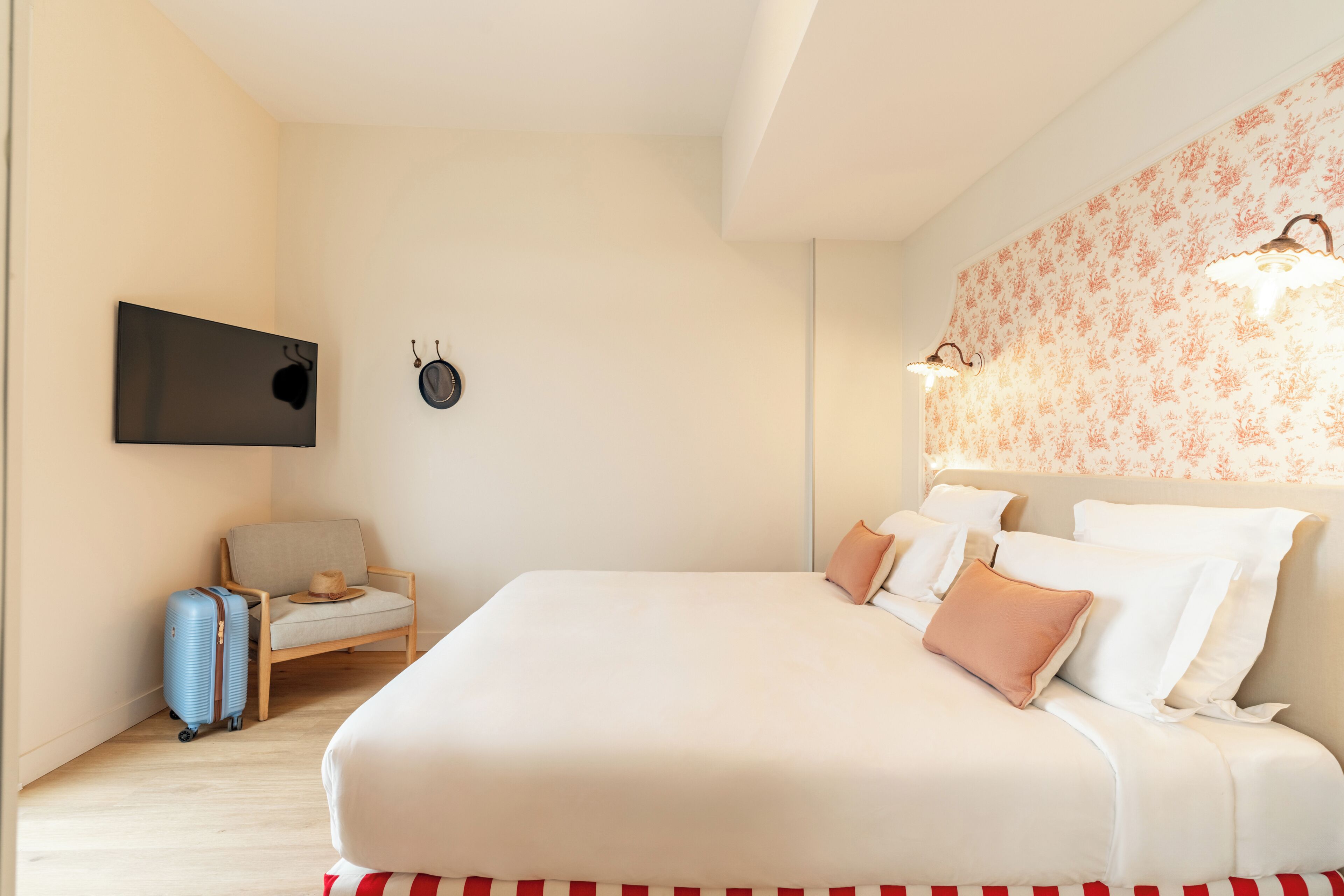 Ein Hotelzimmer mit einem großen Bett, einem Sessel, einem Flachbildfernseher und einem Koffer.