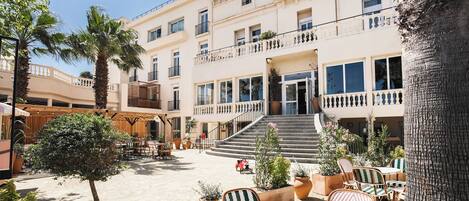 A courtyard with outdoor seating, palm trees, and a building with multiple balconies and windows.