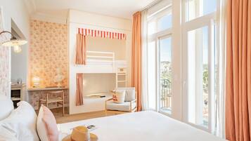 Habitación de hotel con literas, un escritorio con lámpara, una silla, una cama con almohadas y vistas a través de amplios ventanales.
