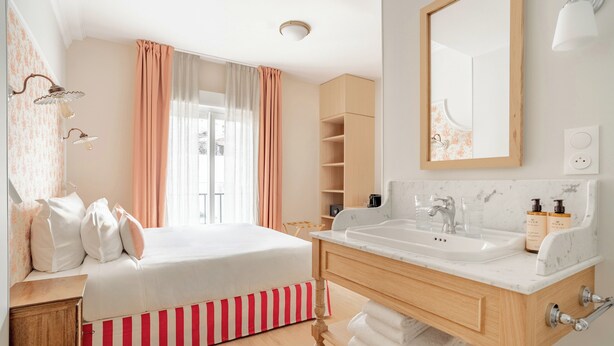 A hotel room with a bed, a bathroom with a sink and mirror, and a window with curtains.