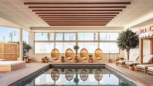 A modern indoor pool area with a wooden deck, lounge chairs, and potted plants.