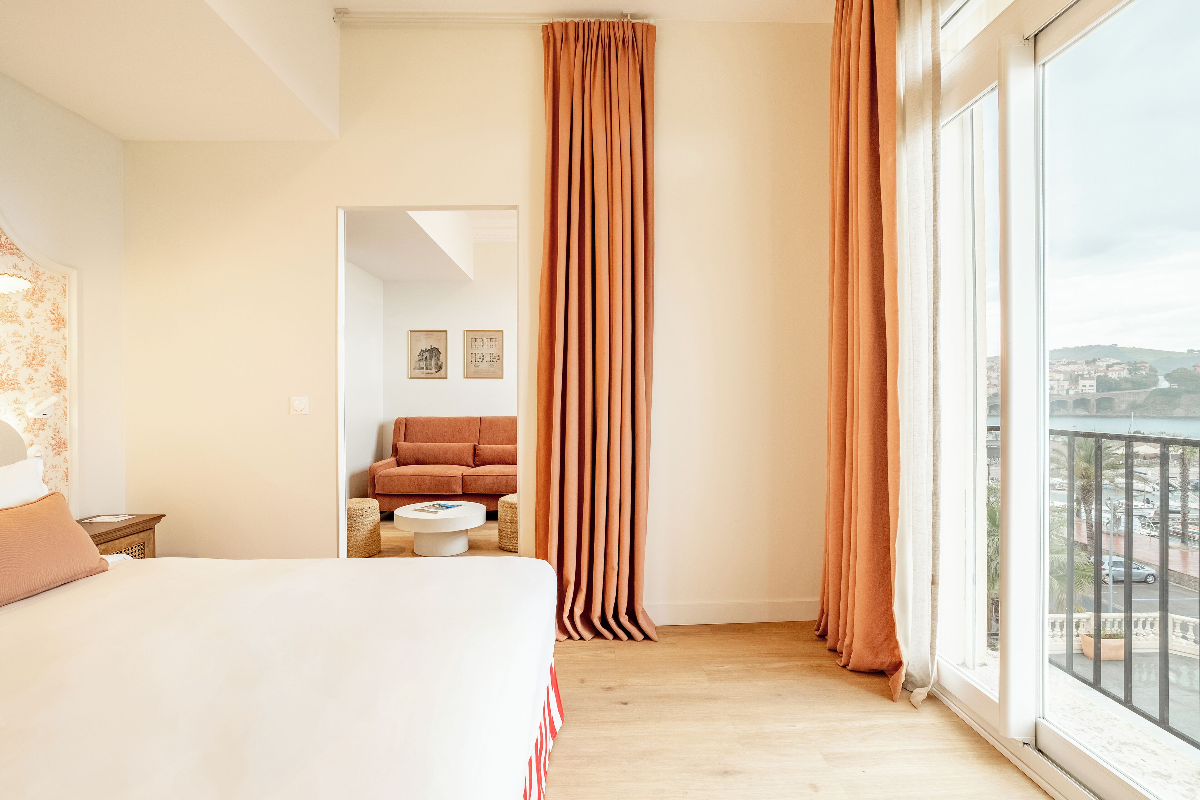 A hotel room with a large bed, a sofa, a coffee table, and a view of a cityscape through a window.
