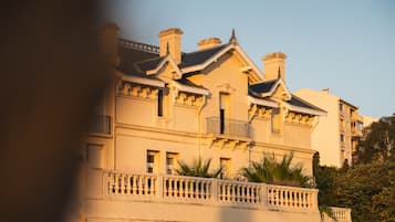 Um edifício grande, com vários andares e estilo arquitetônico clássico, apresentando uma varanda com grades e várias chaminés.