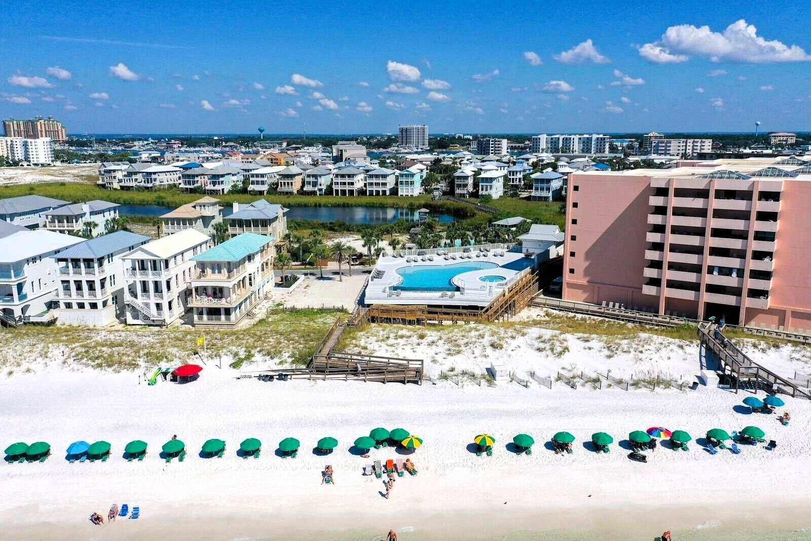 A coastal resort with multiple buildings, a large pool, and beach umbrellas.