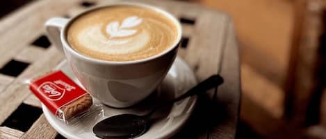 Una taza de café con arte de latte sobre un plato, una cuchara y una galleta sobre una mesa.