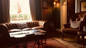 A cozy living room with a leather sofa, a wooden chair, a small table, and a clock on the wall. - The Kings Head (Holt)