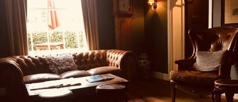 A cozy living room with a leather sofa, a wooden chair, a small table, and a clock on the wall.