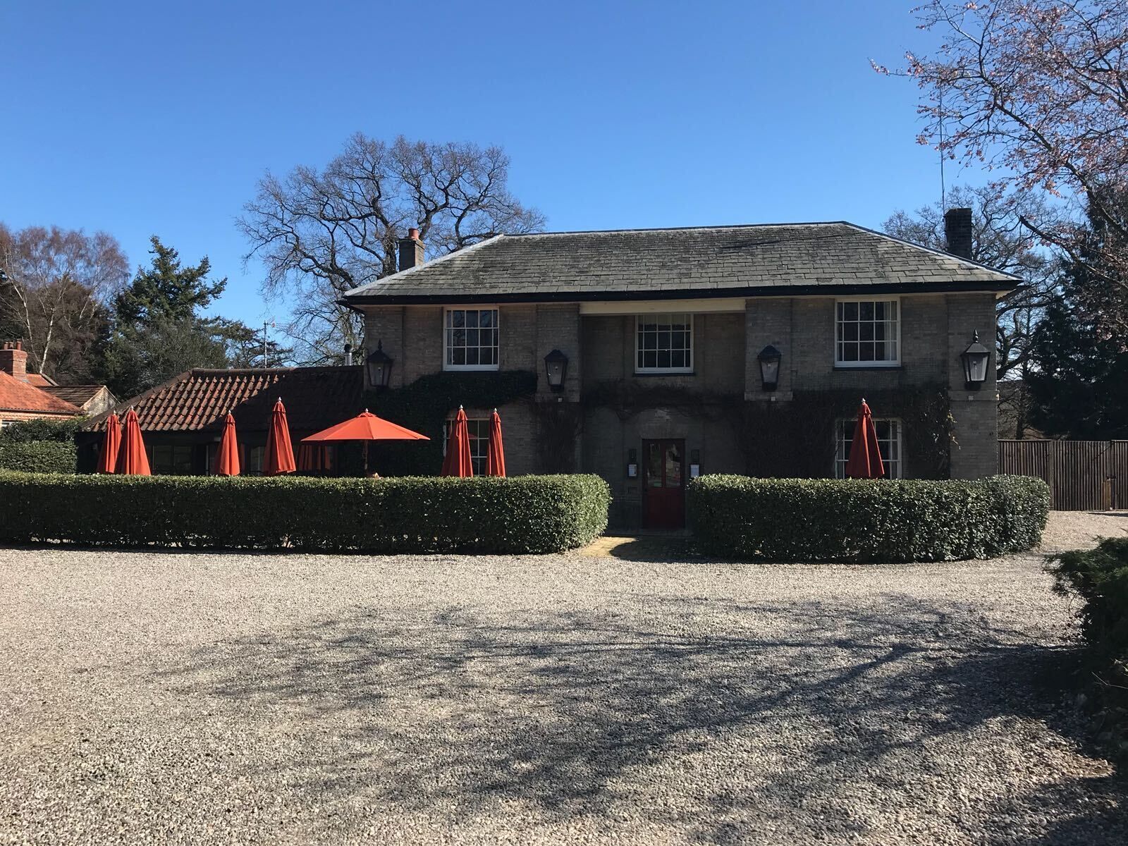 A two-story stone building with a gravel driveway and red umbrellas.