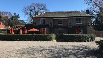 A two-story stone building with a gravel driveway and red umbrellas.