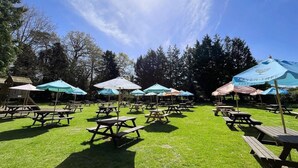 An outdoor picnic area with tables and umbrellas, surrounded by trees. - The Kings Head (Holt)