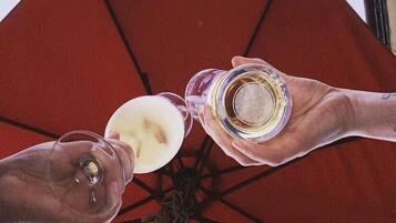 Dos manos sosteniendo vasos de una bebida blanca, posiblemente café, bajo un paraguas rojo.