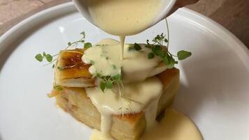 A hand pouring sauce over a dish with a piece of bread and greens.