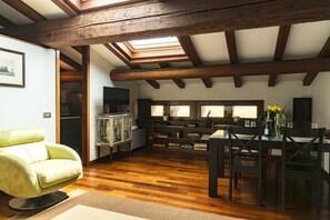 Ruime kamer met houten balken, dakraam, een eethoek met tafel en stoelen, en een groene fauteuil.