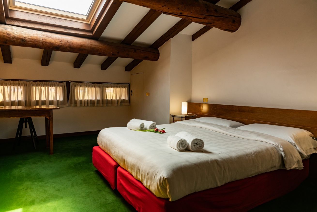 Una camera d'albergo con soffitto in legno, un letto con lenzuola bianche, una scrivania e un tappeto verde.