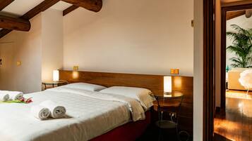 Habitación de hotel con techo de madera, una cama con sábanas blancas, dos mesitas de noche con lámparas y vistas a una planta a través de una puerta abierta.