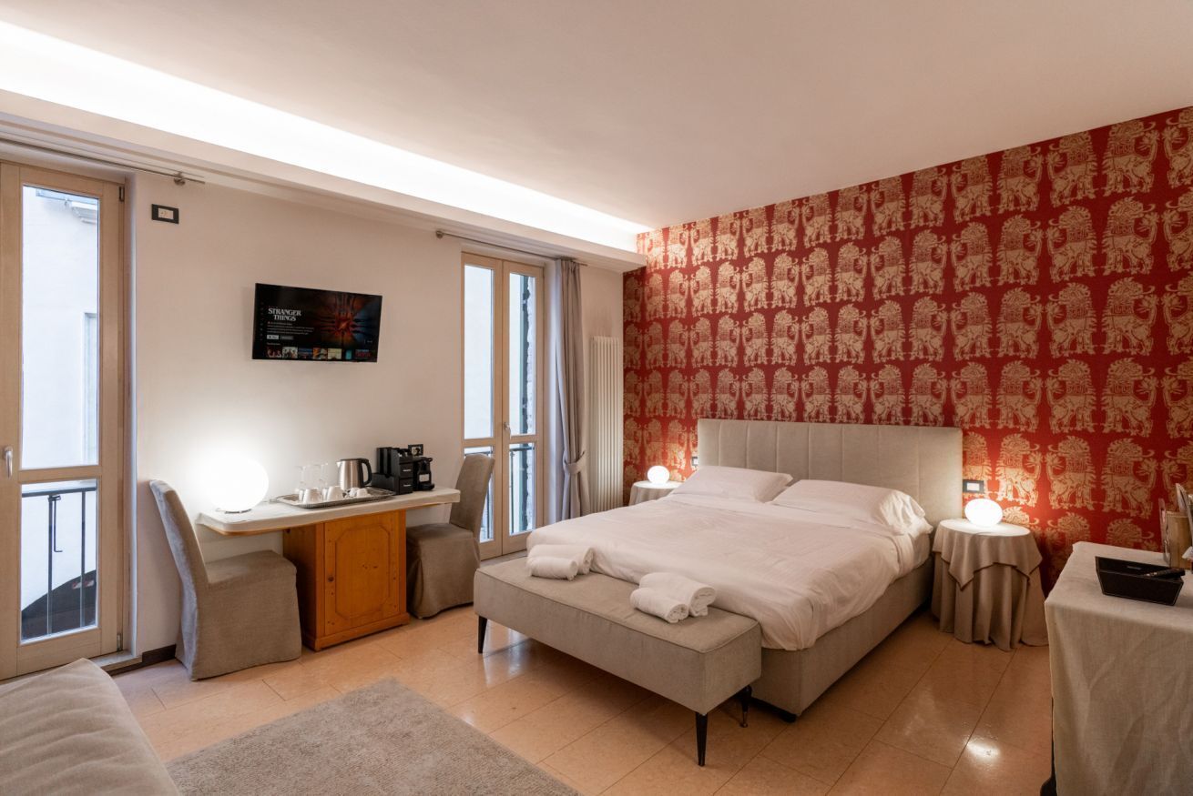 A hotel room with a bed, a desk, a chair, a small table, and a window.