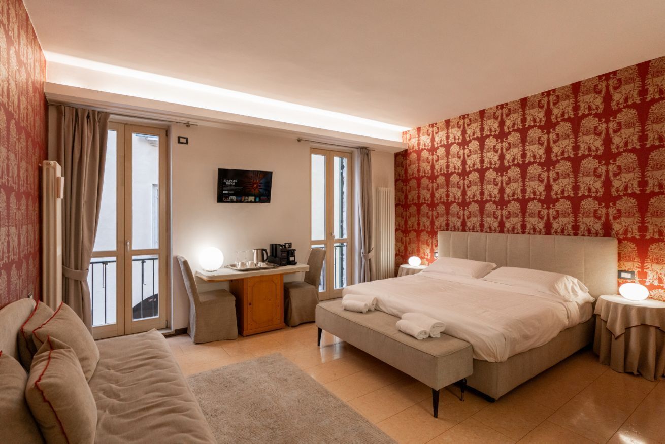 Ein Hotelzimmer mit einem Bett, einem Schreibtisch, einem Sessel und einer Couch, mit Blick durch die Glastüren.