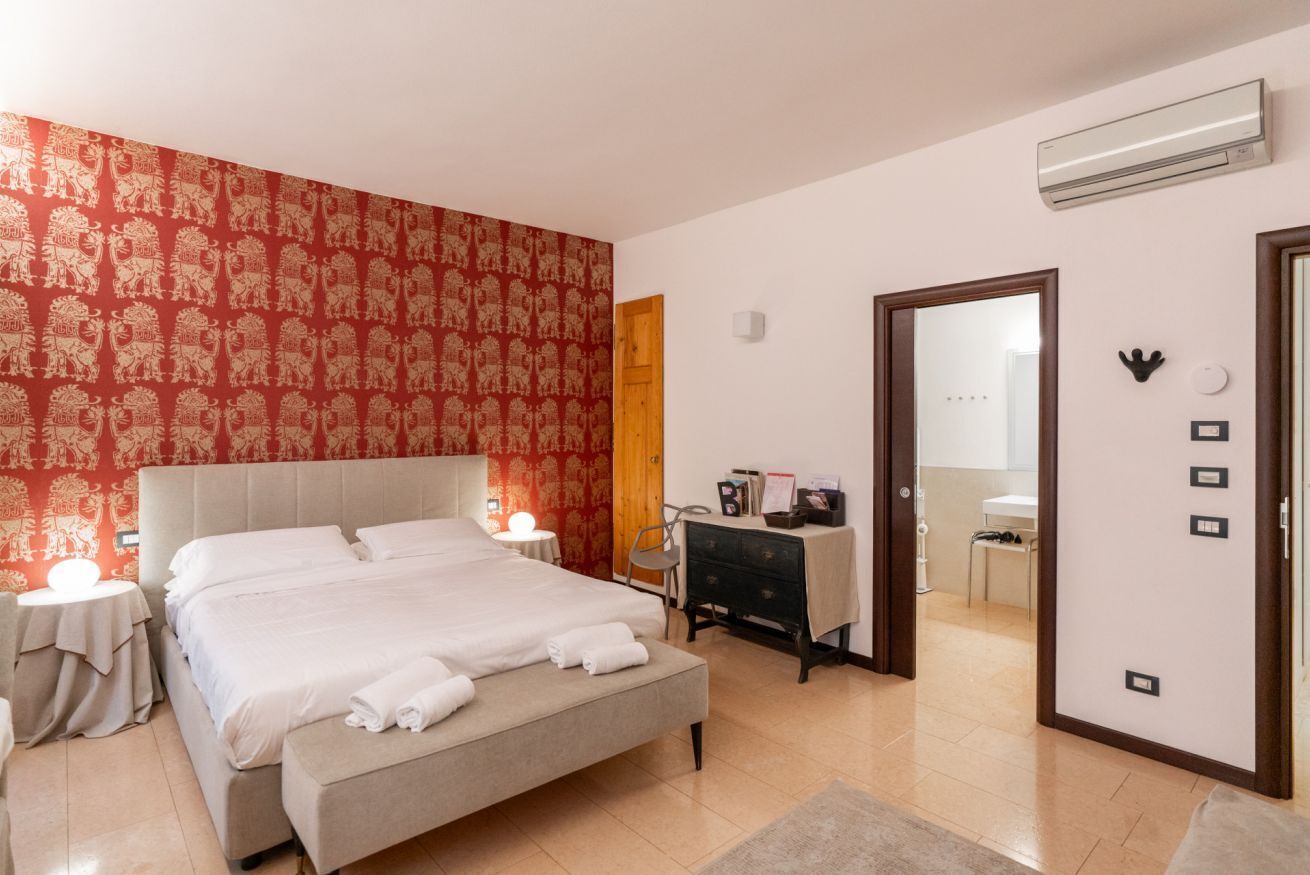 A hotel room with a large bed, a bedside table, a dresser, a mirror, and a door leading to a bathroom.