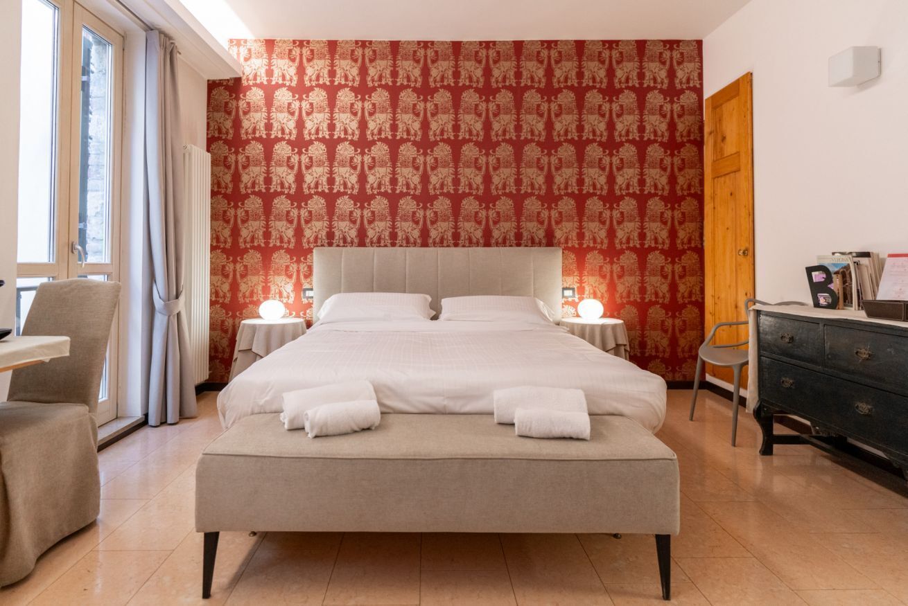 Ein Hotelzimmer mit einem großen Bett, zwei Nachttischen, einem Sessel, einer Kommode und einem Fenster mit Vorhängen.