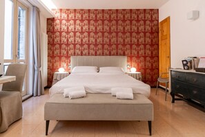 A hotel room with a large bed, two bedside tables, a chair, a dresser, and a window with curtains.