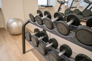 A rack of dumbbells with weights ranging from 2 to 10 kg, a large exercise ball, and a treadmill in the background.