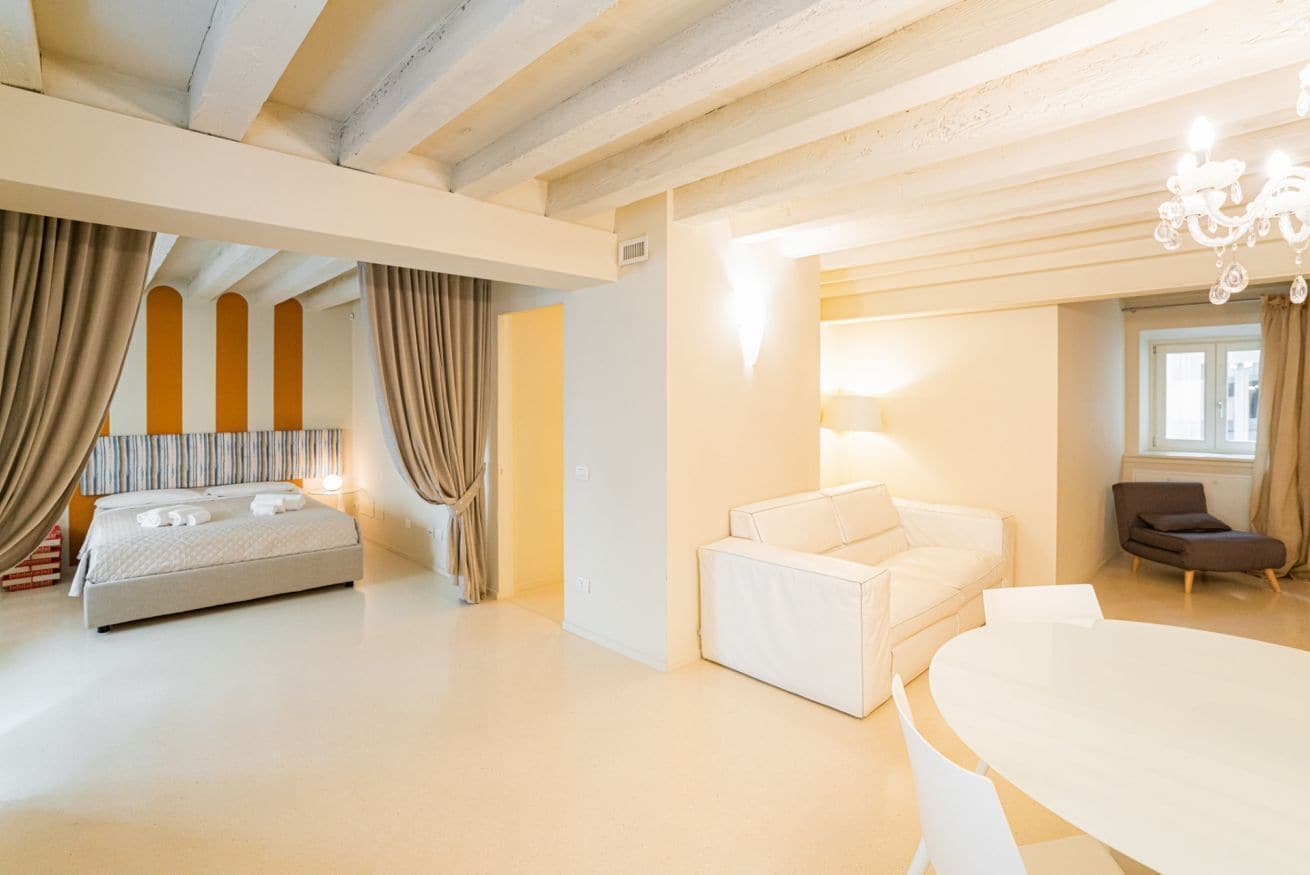 A modern hotel room with a bed, a sofa, a dining table, and a chandelier.