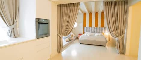 A modern bedroom with a bed, a built-in oven, and a window with curtains.