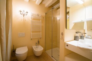 Ein Badezimmer mit Toilette, Bidet, Duschkabine aus Glas und einem Waschbecken mit Spiegel.