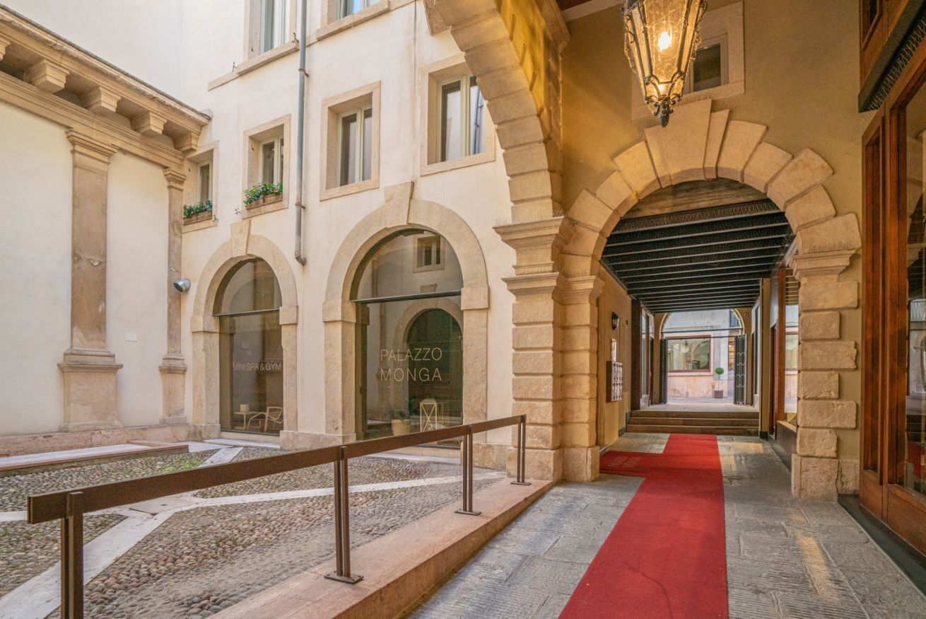 A hotel corridor with a red carpet, stone arches, and a sign for 'Palazzo Monga' spa and gym.
